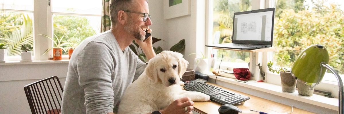 A person talking on the phone while sitting at a home office desk with a puppy in their lap.