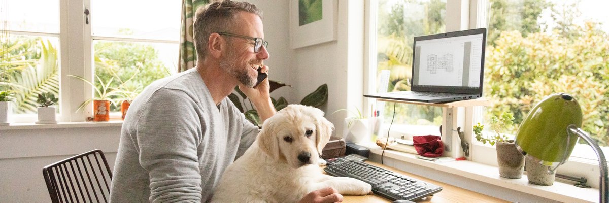 A person talking on the phone while sitting at a home office desk with a puppy in their lap.