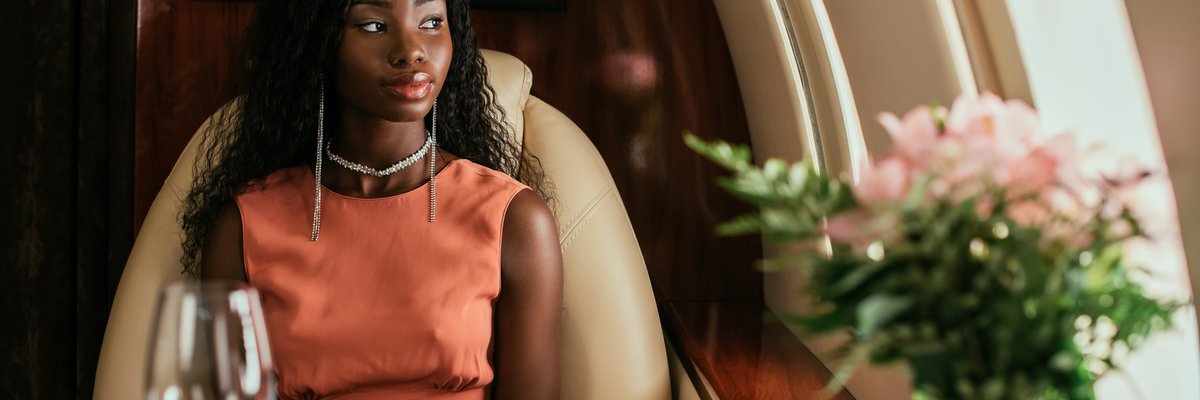 A person looking out the window while sitting at a table set with white linen and flowers on a private plane.
