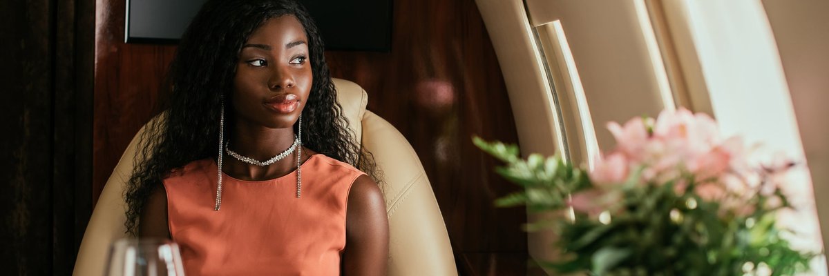 A person looking out the window while sitting at a table set with white linen and flowers on a private plane.