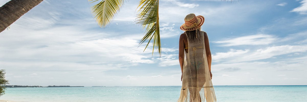 A person standing under a palm tree on a tropical beach.