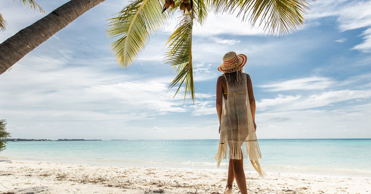 A person standing under a palm tree on a tropical beach.