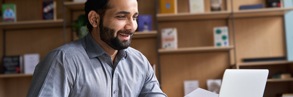 A smiling person on a video call with their laptop in a home office.