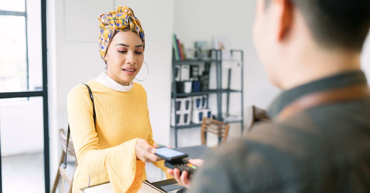A person holding their smartphone over a payment reader held out by a shop employee.