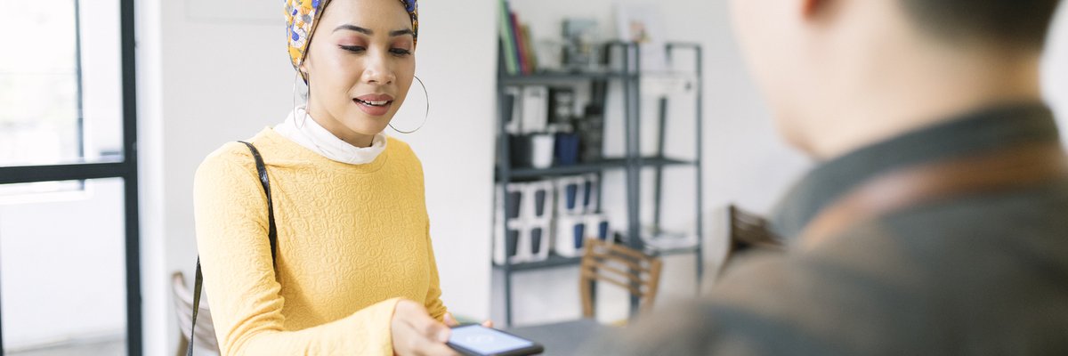 A person holding their smartphone over a payment reader held out by a shop employee.