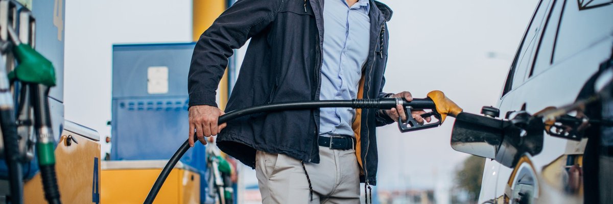 A person standing next to their car pumping gas at a gas station.
