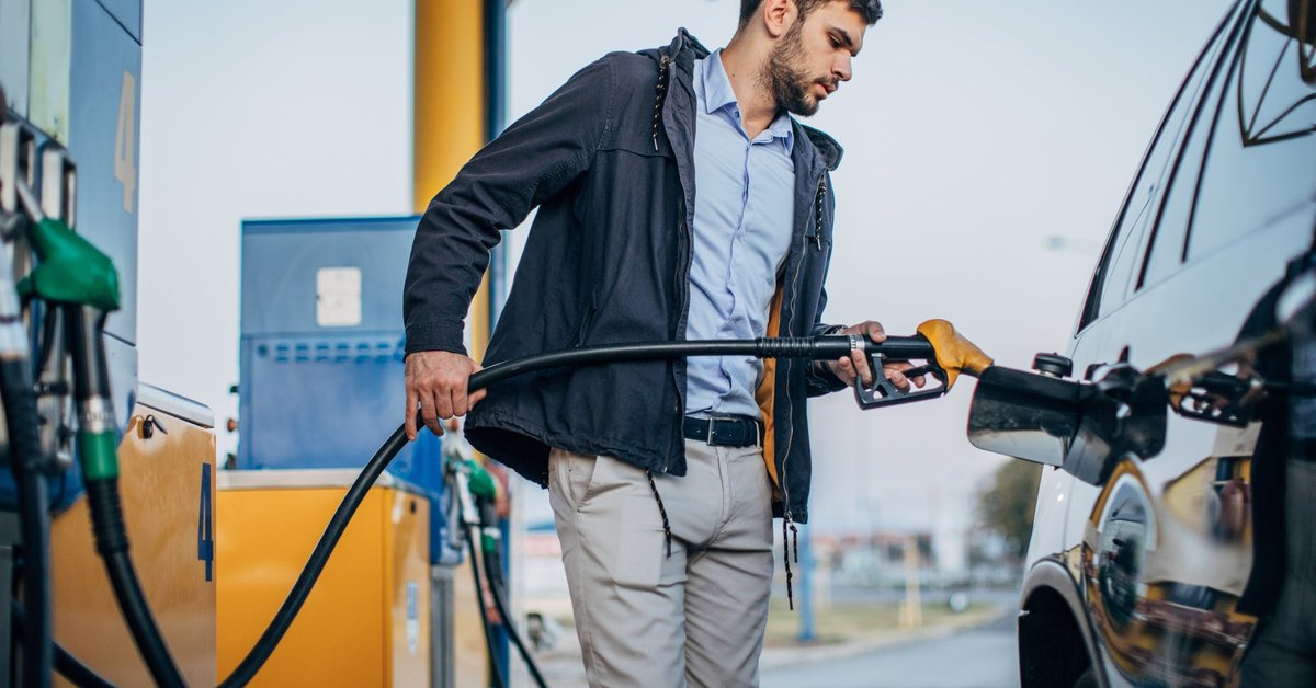 A person standing next to their car pumping gas at a gas station.