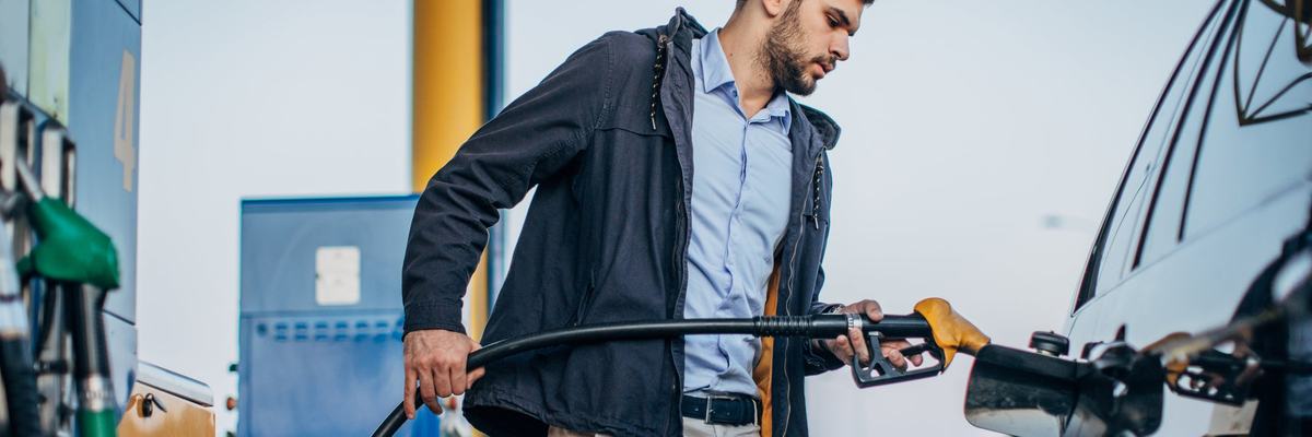 A person standing next to their car pumping gas at a gas station.