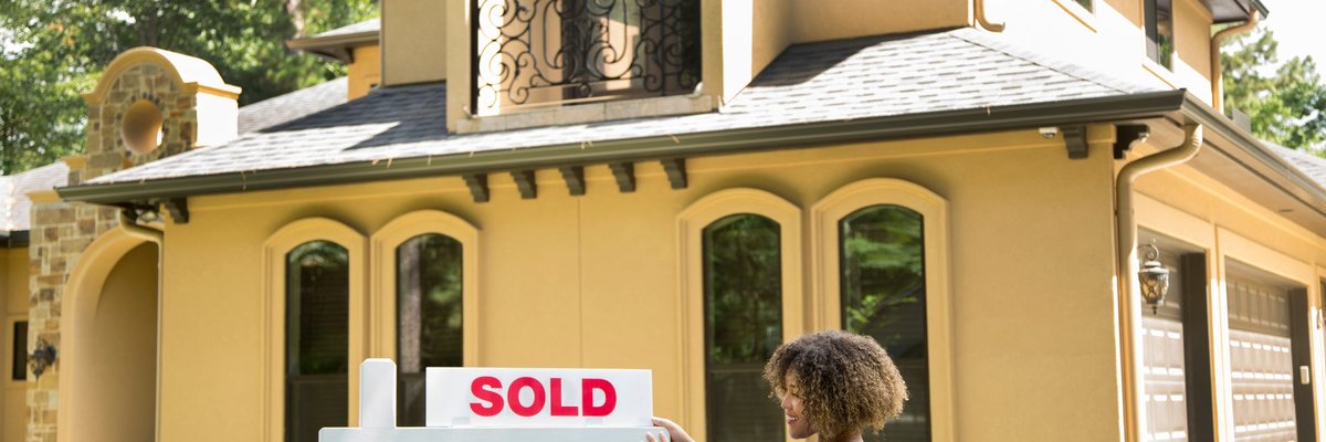 A person hanging a Sold sign on top of a For Sale sign in front of a home.