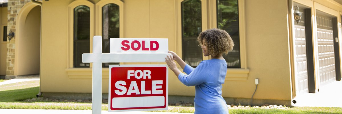 A person hanging a Sold sign on top of a For Sale sign in front of a home.