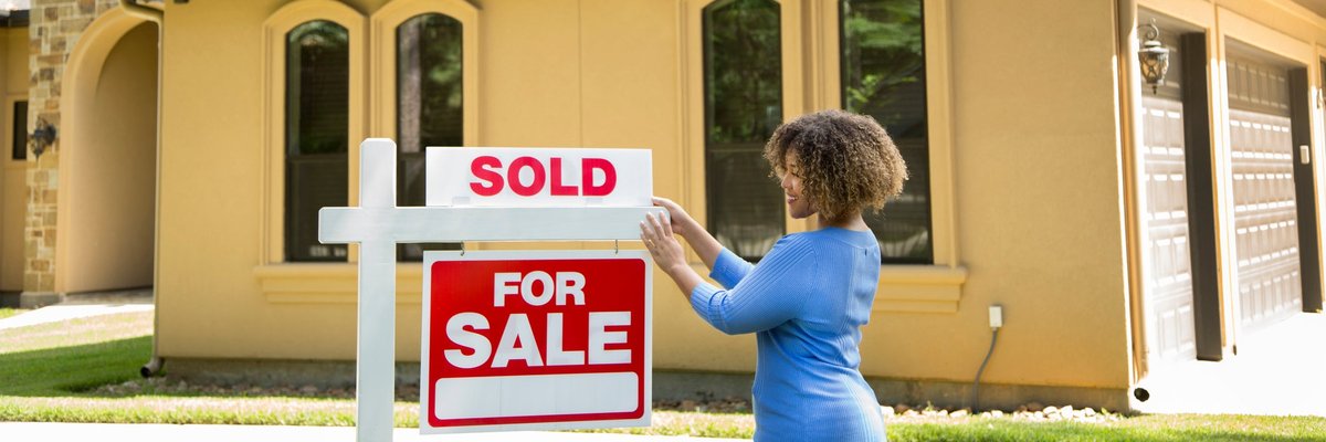 A person hanging a Sold sign on top of a For Sale sign in front of a home.