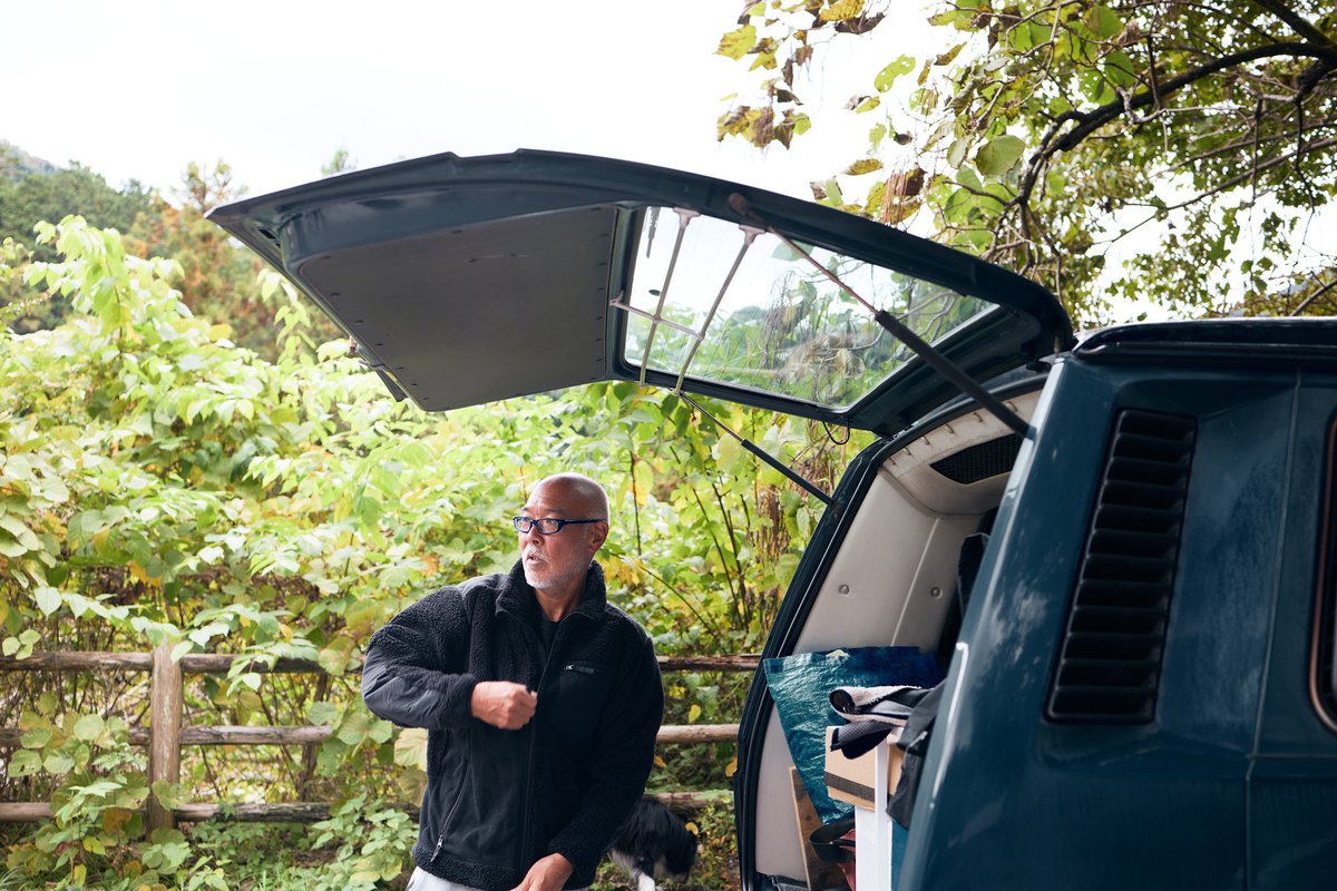 A person standing next to the open trunk door of a car and zipping up their jacket.