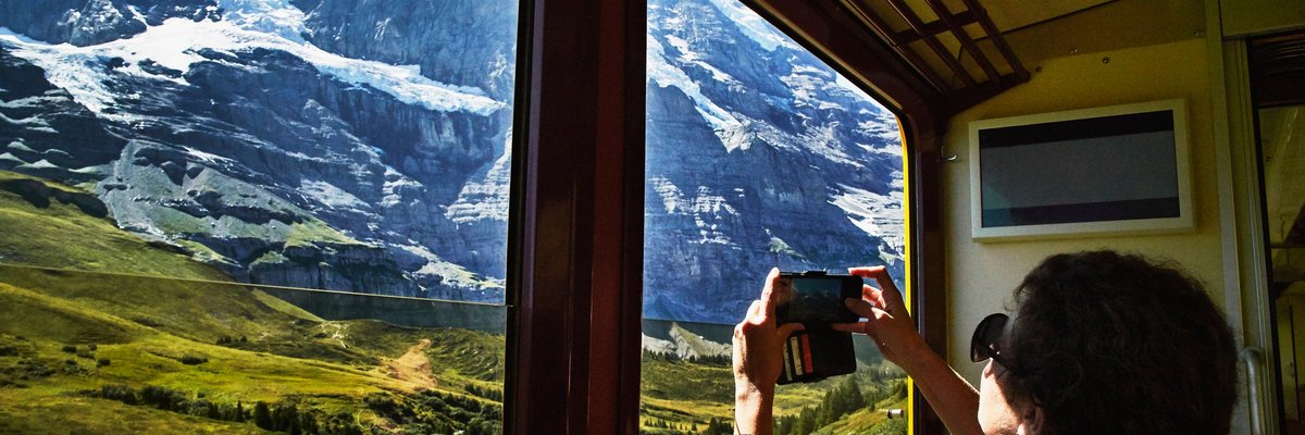 A person taking a photo of a snowy mountain peak through a train window.