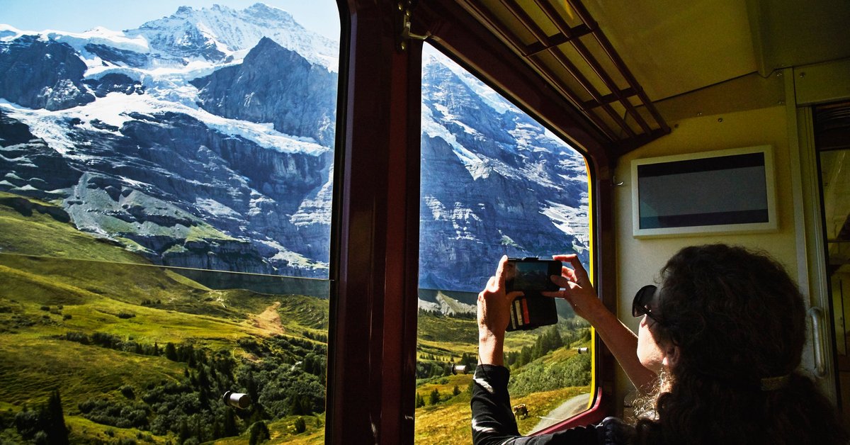 A person taking a photo of a snowy mountain peak through a train window.