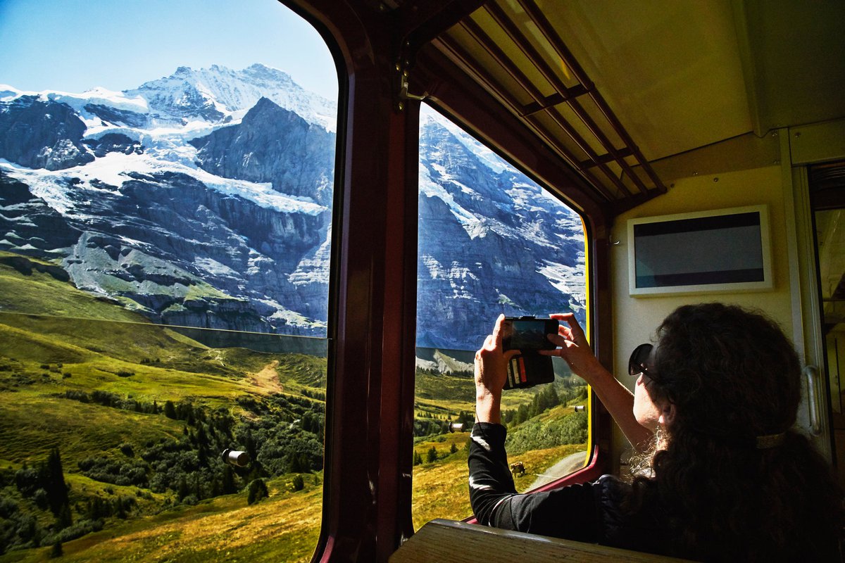A person taking a photo of a snowy mountain peak through a train window.