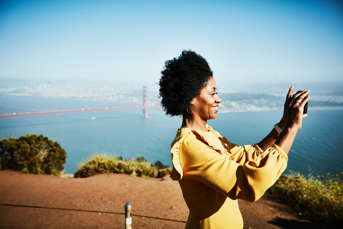 A person taking a photo at a lookout point over the ocean with the Golden Gate Bridge in the background.
