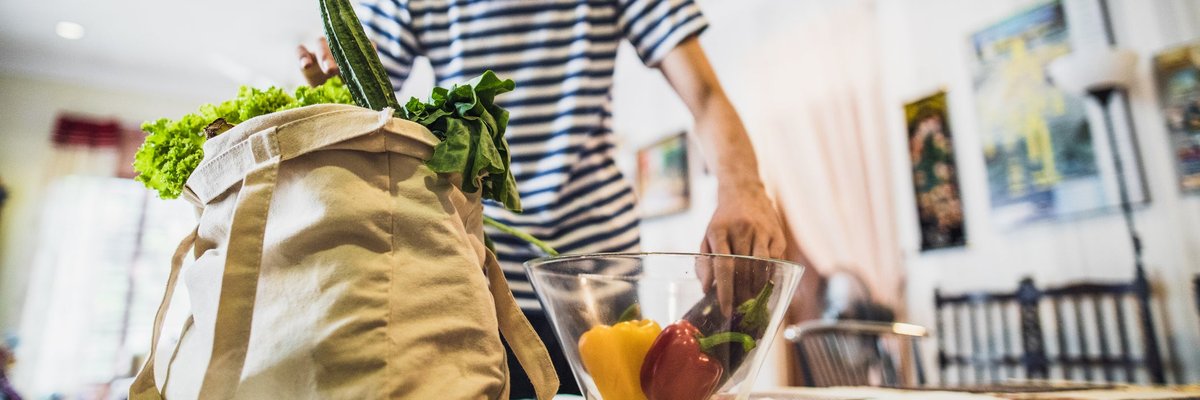 A person unpacking fruits from a grocery bag into a bowl on the dining room table.