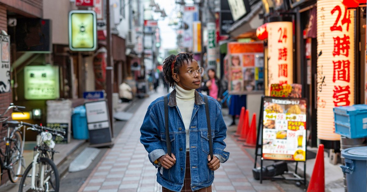 A traveler wearing a backpack and walking down a small street lined with shops and restaurants in Tokyo.