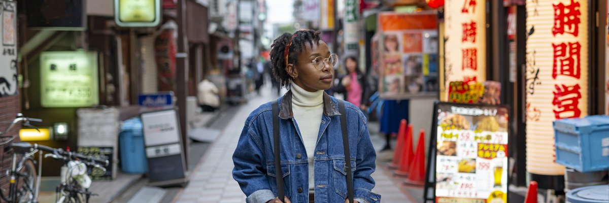 A traveler wearing a backpack and walking down a small street lined with shops and restaurants in Tokyo.