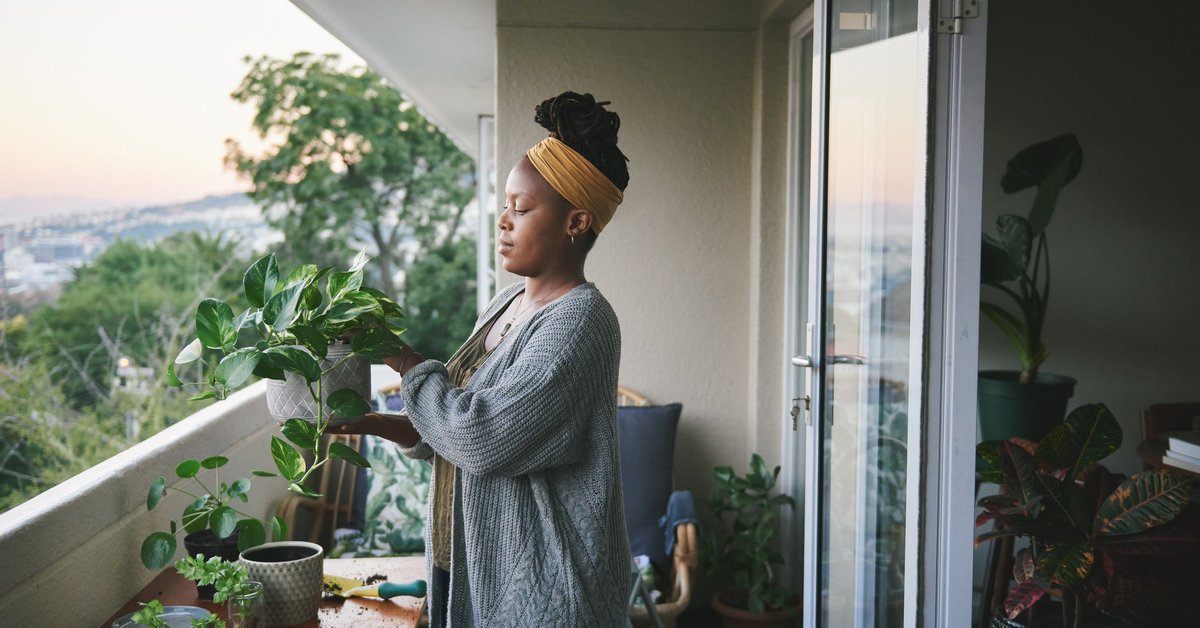 A person standing on a balcony and tending to their houseplants.