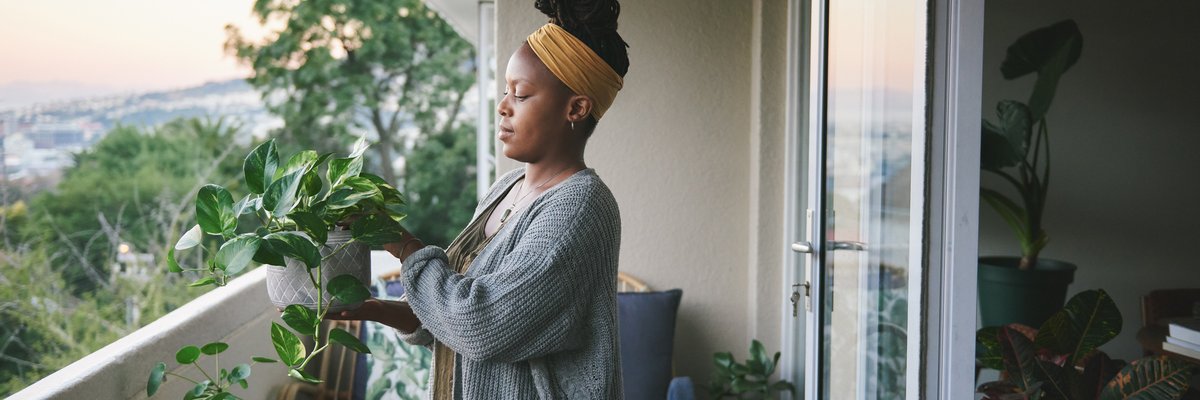 A person standing on a balcony and tending to their houseplants.