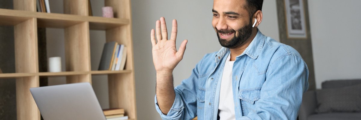 A person working at a desk at home and waving on a video call.