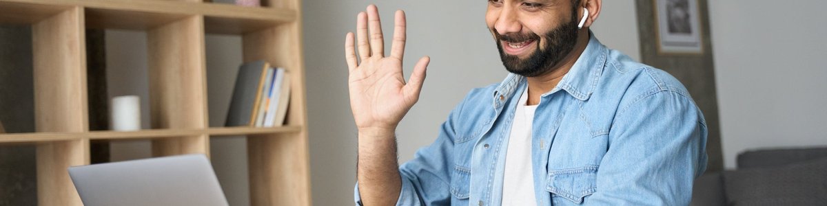 A person working at a desk at home and waving on a video call.