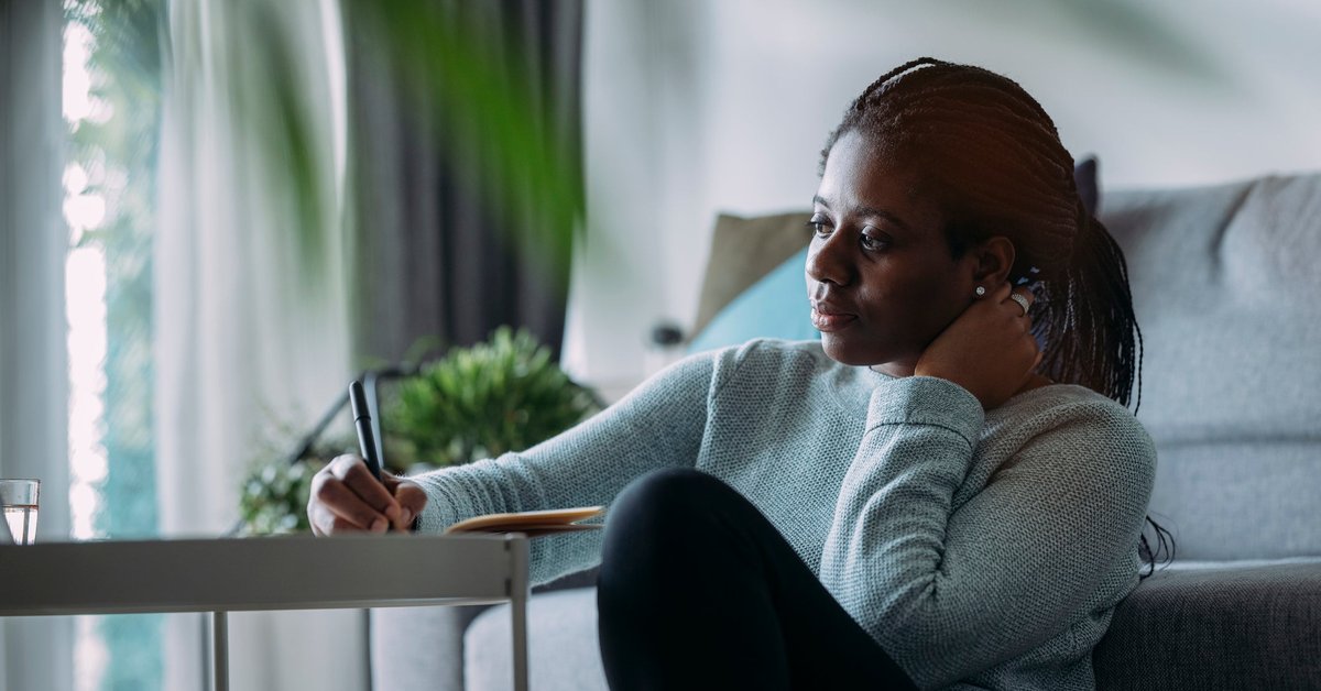 A person sitting at a desk in their living room and writing in a notebook.