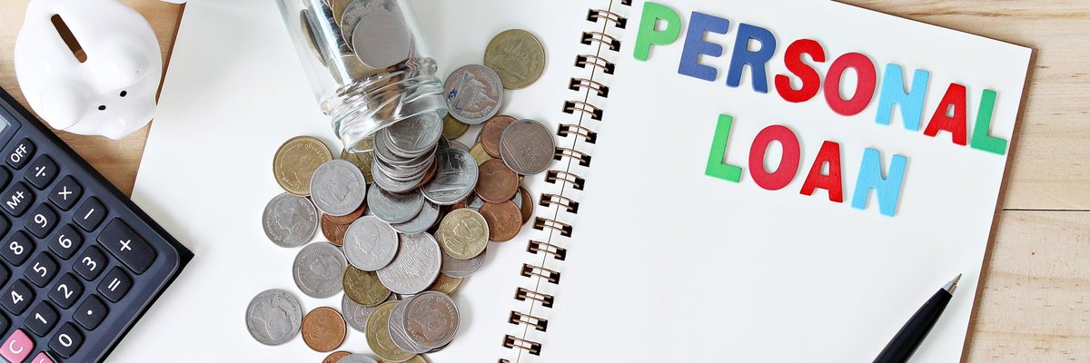 Jar of coins spilling onto a notebook with colorful letters spelling out PERSONAL LOAN