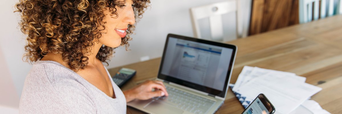 Woman using laptop and phone to track her personal finances.