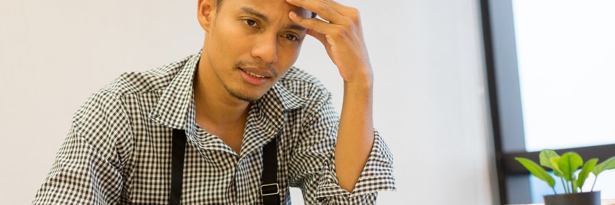 Dismayed man sitting at a desk with his hand on his forehead.