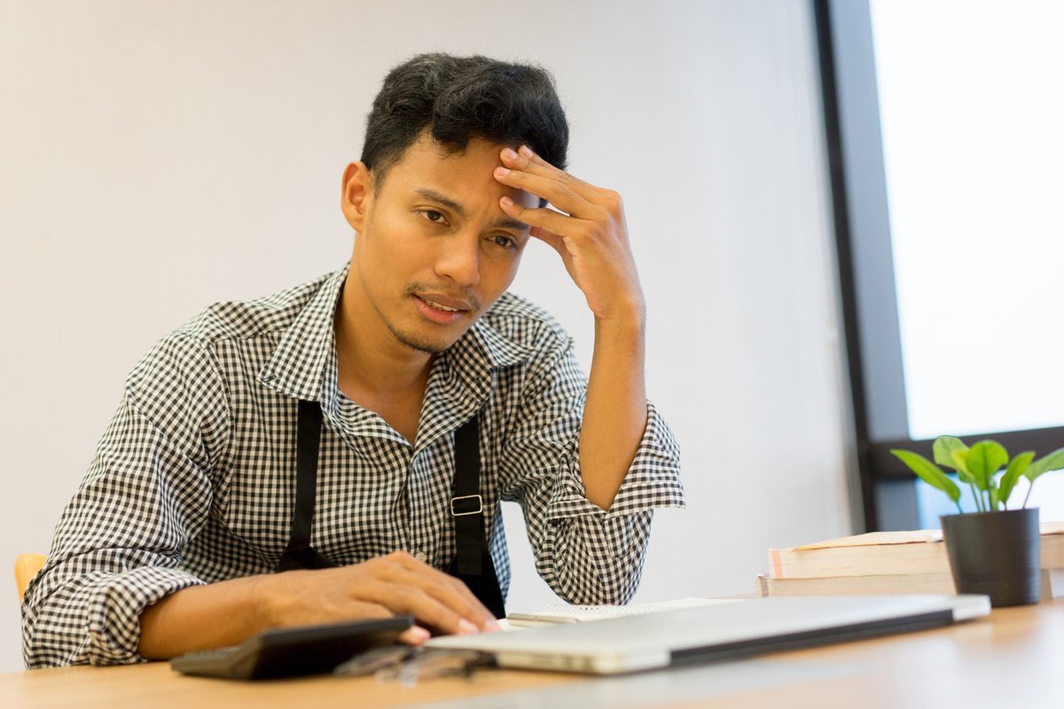 Dismayed man sitting at a desk with his hand on his forehead.