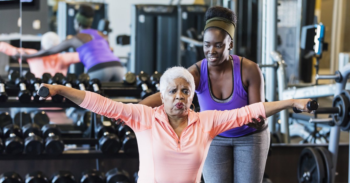 Senior citizen works out in a gym with a personal trainer.
