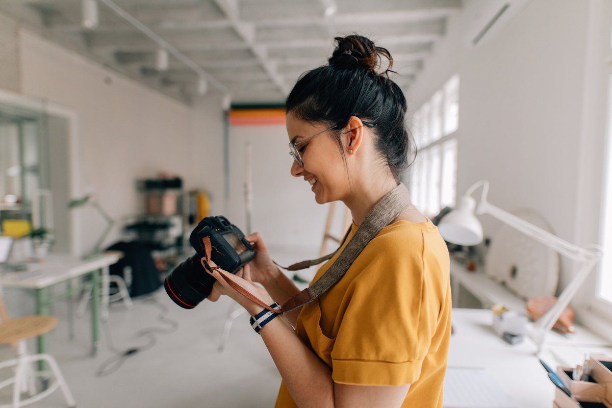 A smiling photographer standing in a loft studio and looking at the screen on the camera in their hands.