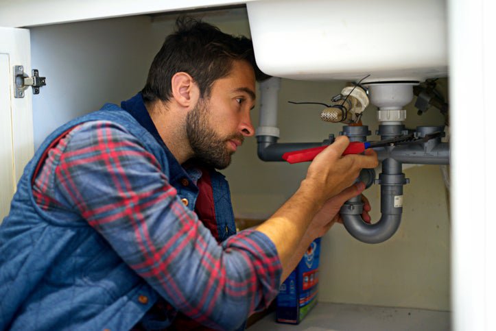 A plumber working on the pipes under a sink.