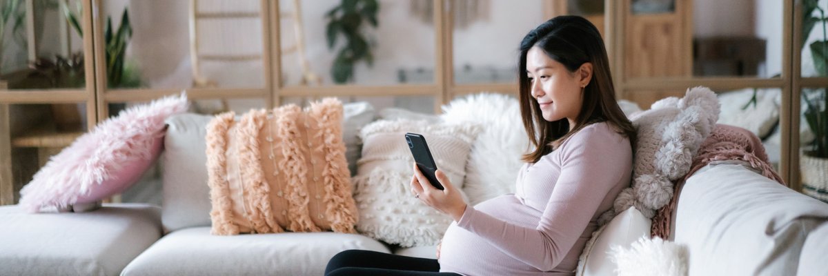 A pregnant person sitting on their couch and looking at their phone.
