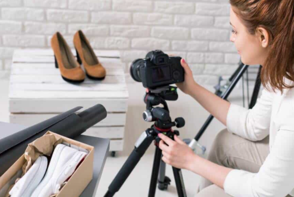 Photo of a woman using a tripod to photograph shoes.