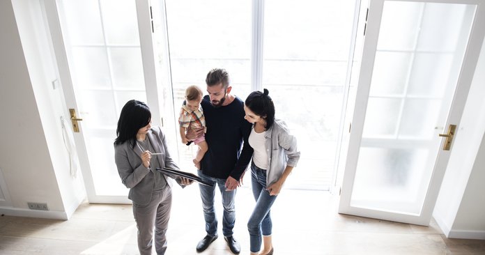 A real estate agent shows a couple with an infant a house.
