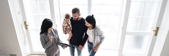 A real estate agent shows a couple with an infant a house.