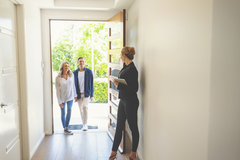 A realtor opening the door of a new home for a young couple.