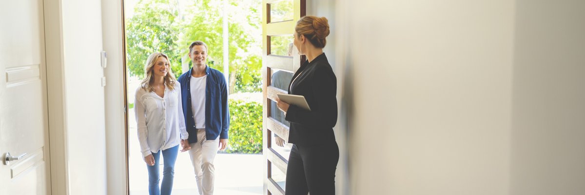 A realtor opening the door of a new home for a young couple.