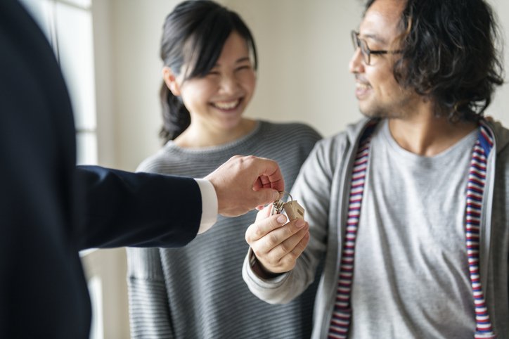 A realtor handing a set of house keys to a smiling man and woman.