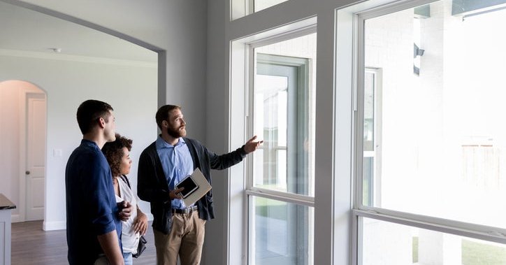 A realtor walking his clients through an empty house and pointing out the window.