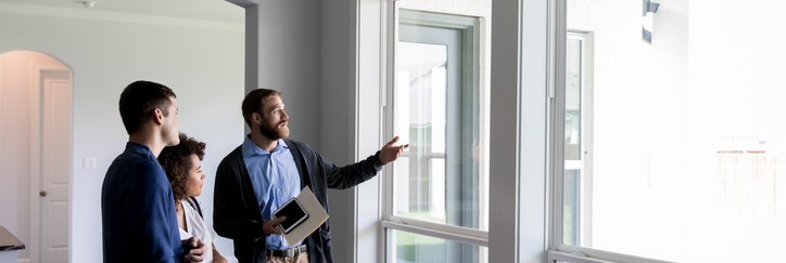 A realtor walking his clients through an empty house and pointing out the window.
