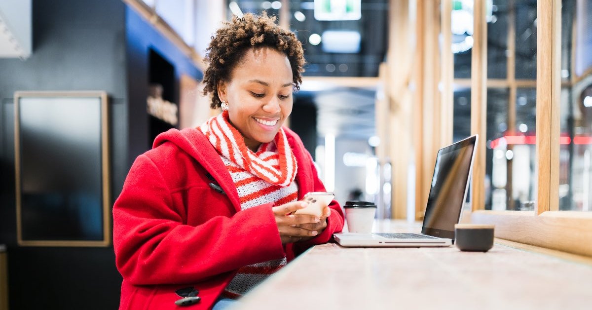 A women at a coffee shop smiling on her phone with her laptop out.