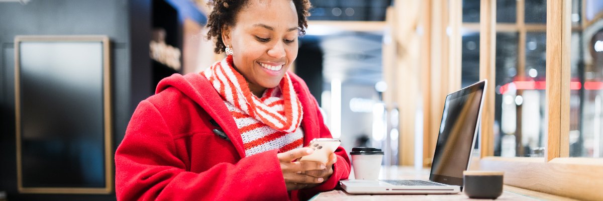 A women at a coffee shop smiling on her phone with her laptop out.