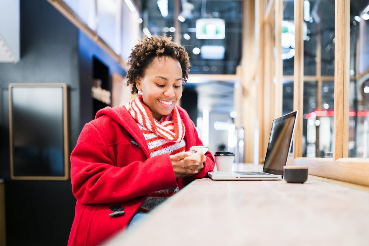 A women at a coffee shop smiling on her phone with her laptop out.