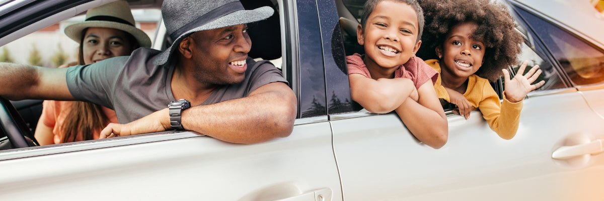 Family of four smiling and waving out of a car.