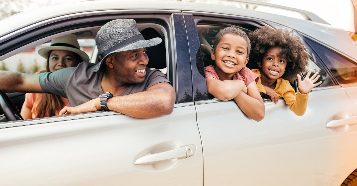 Family of four smiling and waving out of a car.