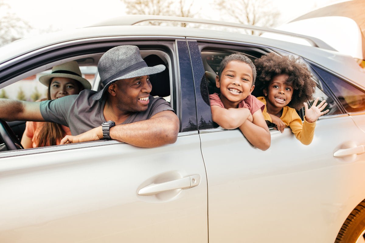 Family of four smiling and waving out of a car.